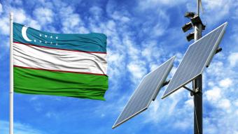 Solar panels on a background of blue sky with a flagpole and the flag of Uzbekistan